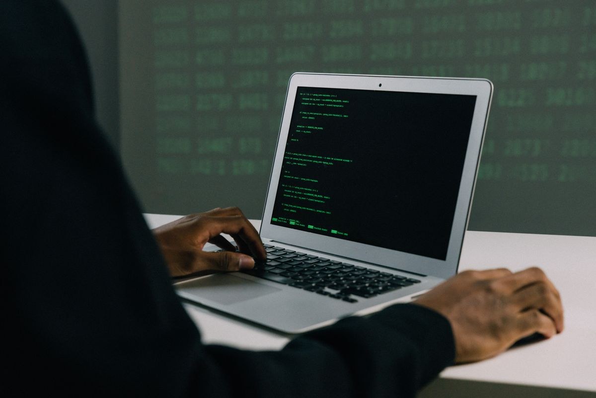 Over-the-shoulder view of a laptop showing green code on a dark desk